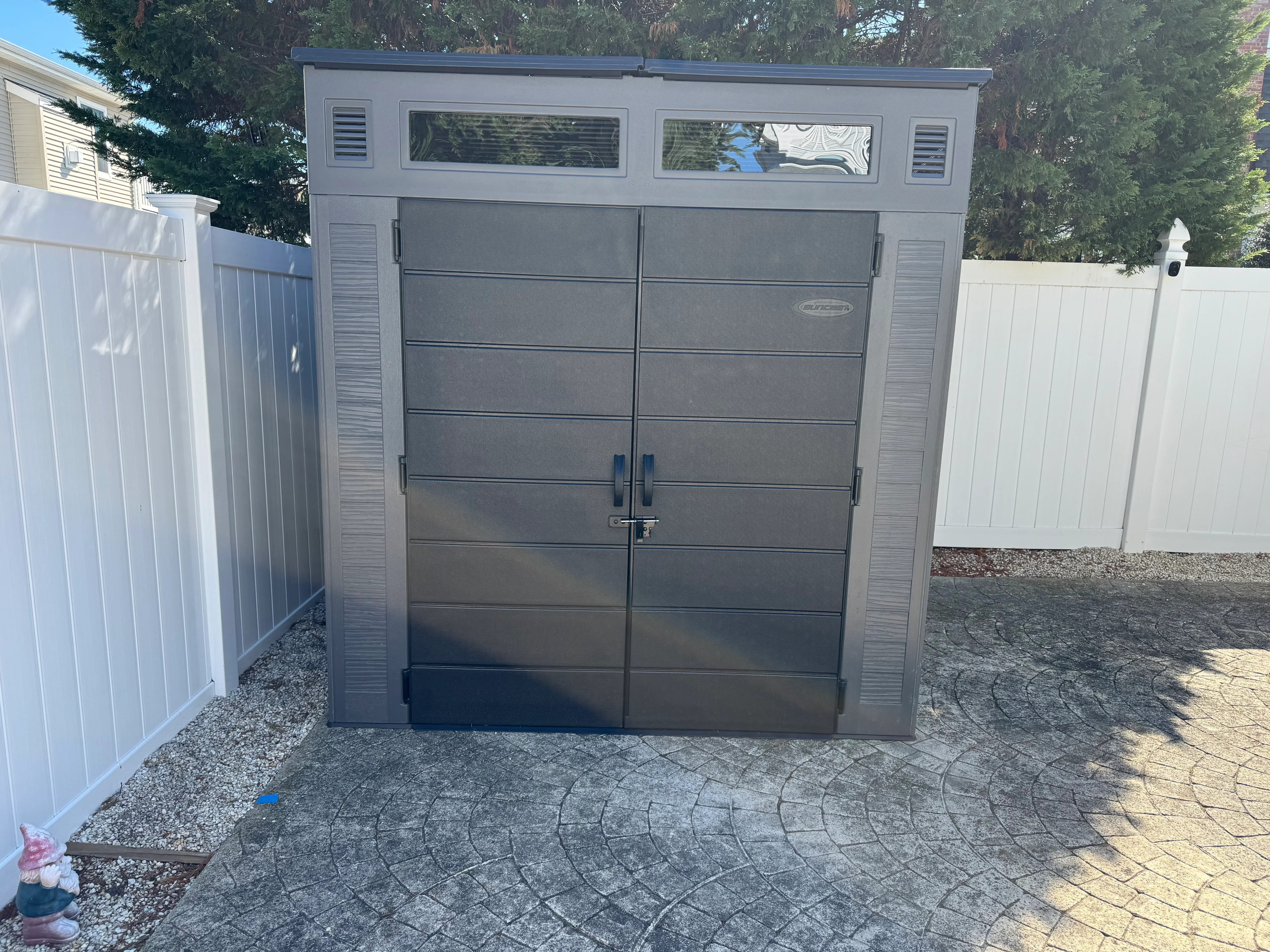 Dark gray modern garage door with horizontal panels and windows installed between white vinyl fencing