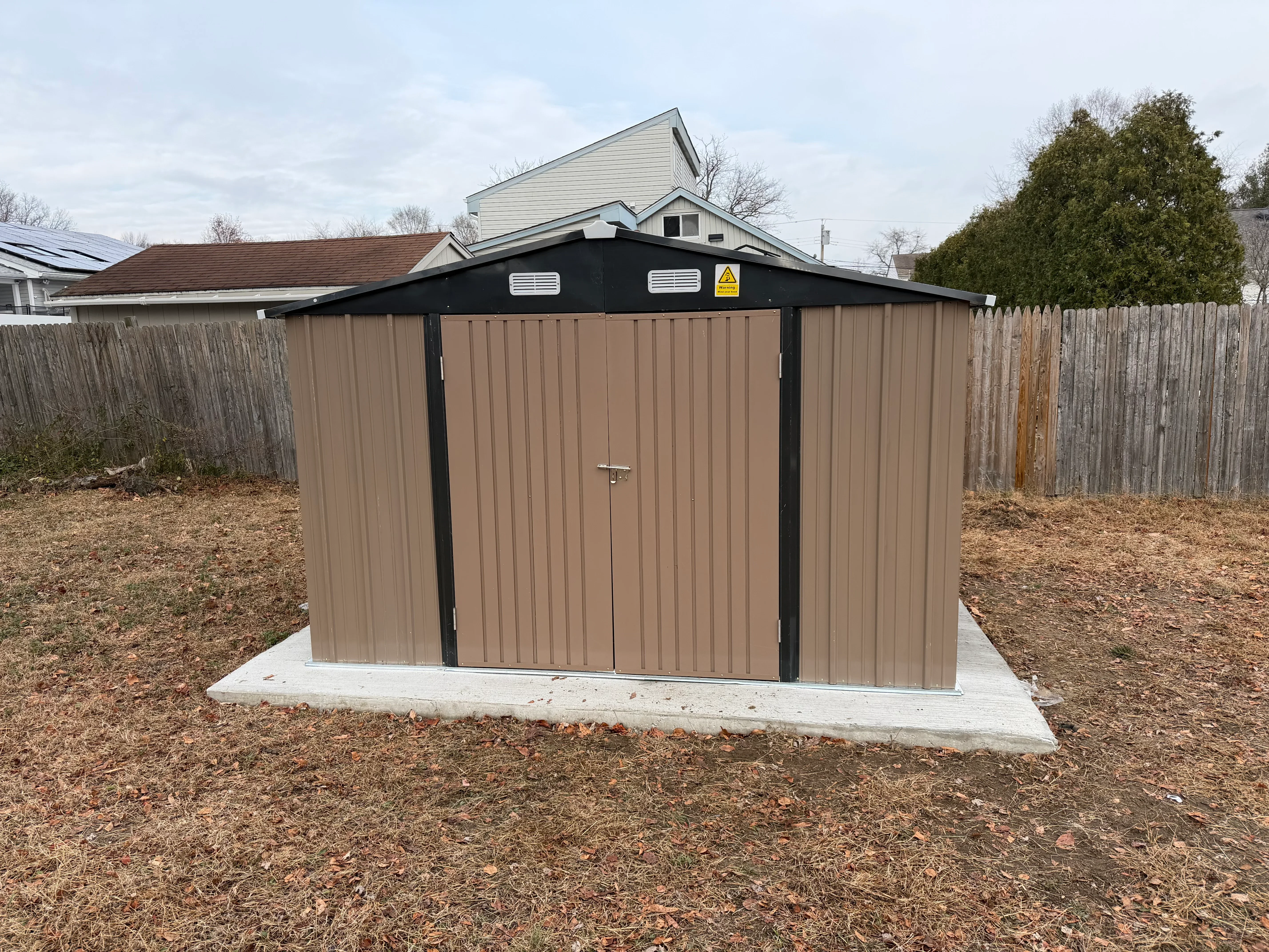Tan and black metal storage shed with corrugated steel walls on concrete foundation