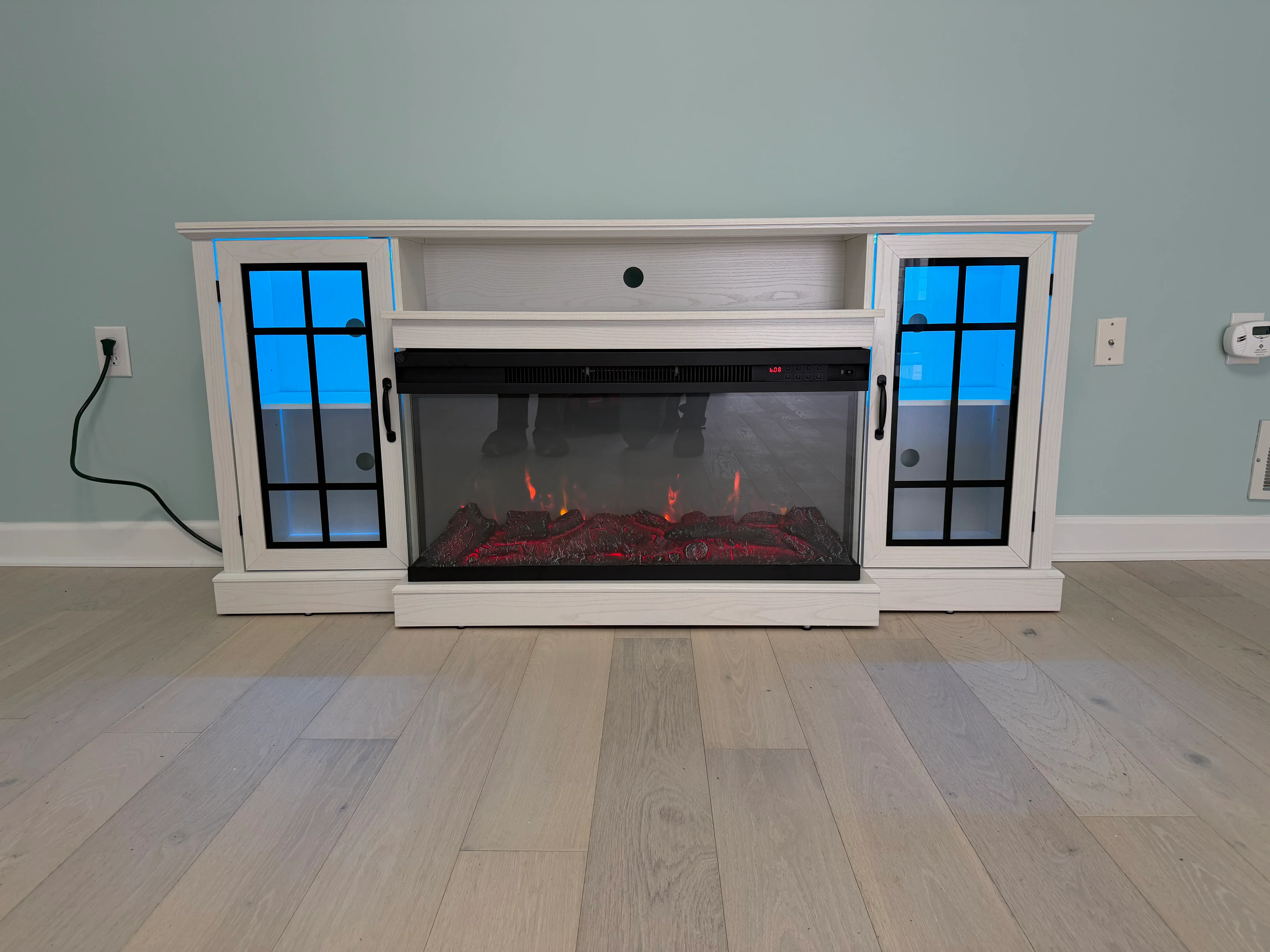 White entertainment center with electric fireplace insert, glass-door cabinets, and realistic flame effect