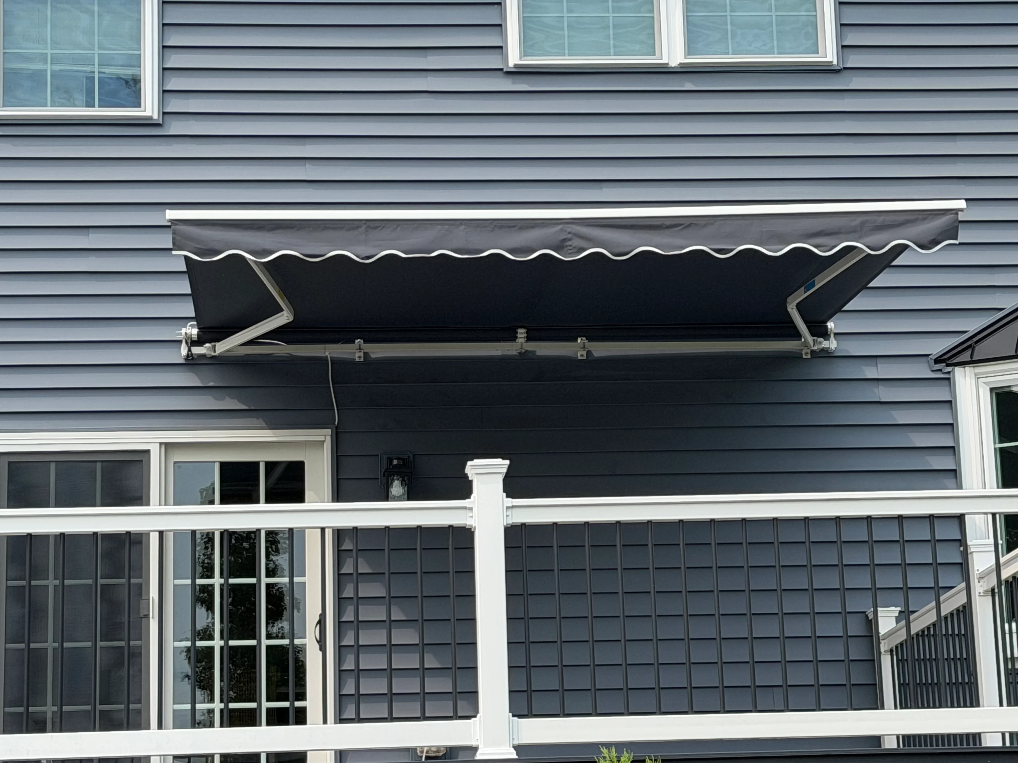 Black retractable awning with white trim installed above deck on gray siding
